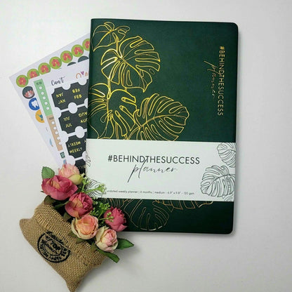 Undated productivity planner with gold leaf design, stickers, and a small flower arrangement