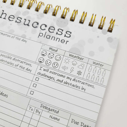 Undated spiral-bound productivity planner with mood, weather, and water tracker sections.