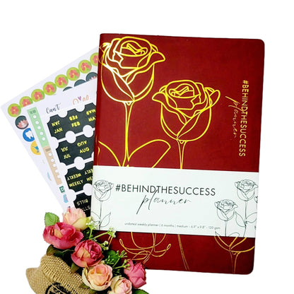 Undated red productivity planner with gold rose design, planner stickers, and pink flowers.