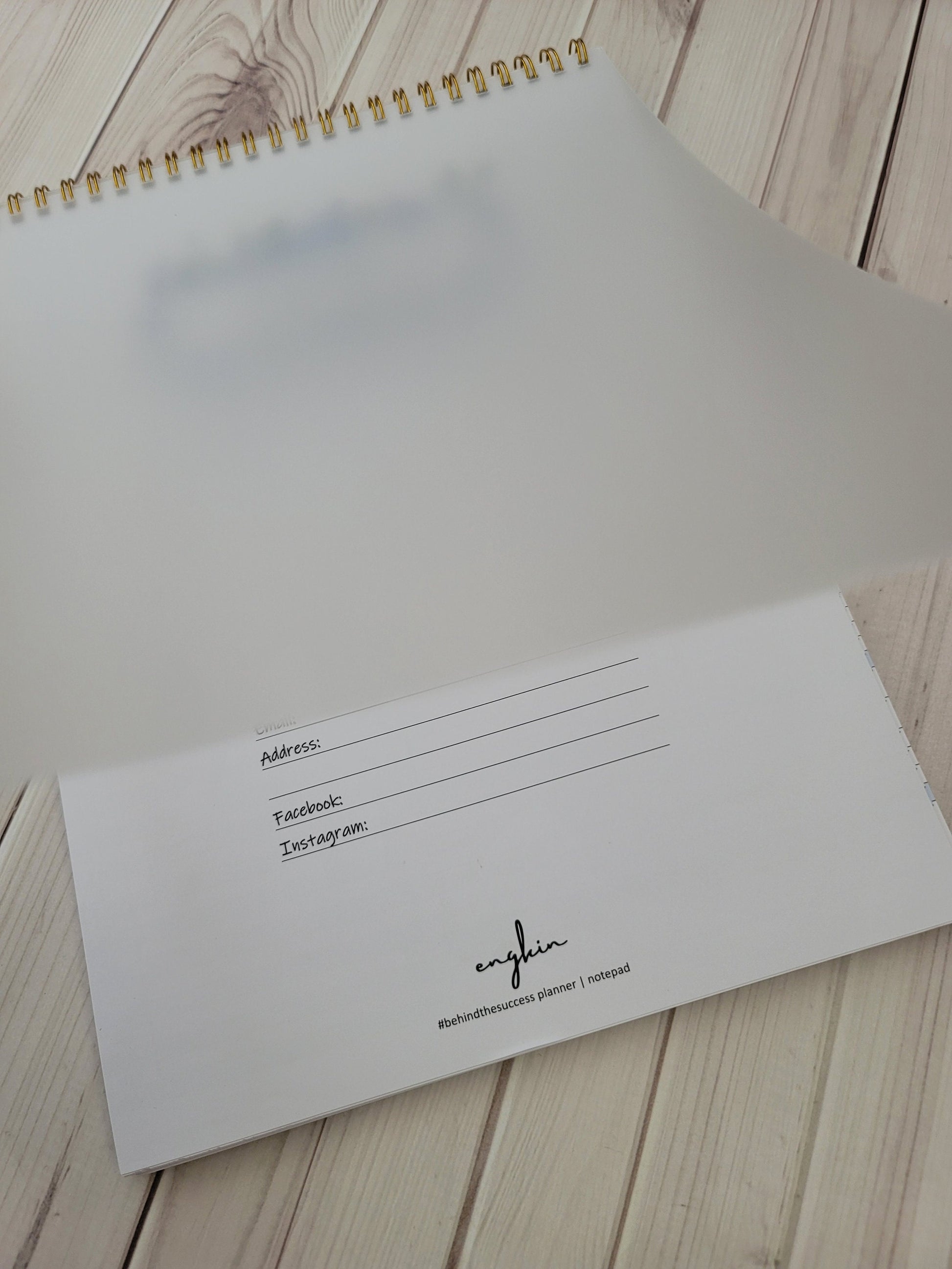 Undated productivity planner with gold spiral binding, open to personal info page on wooden desk.