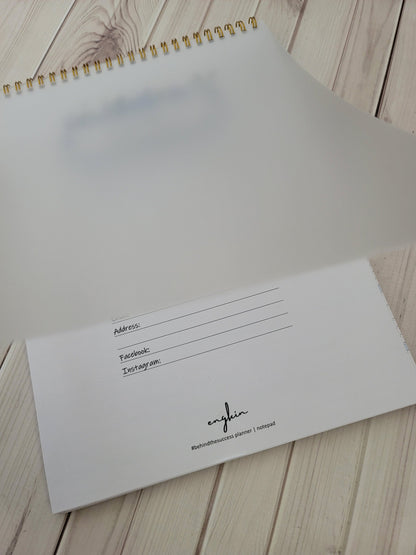 Undated productivity planner with gold spiral binding, open to personal info page on wooden desk.