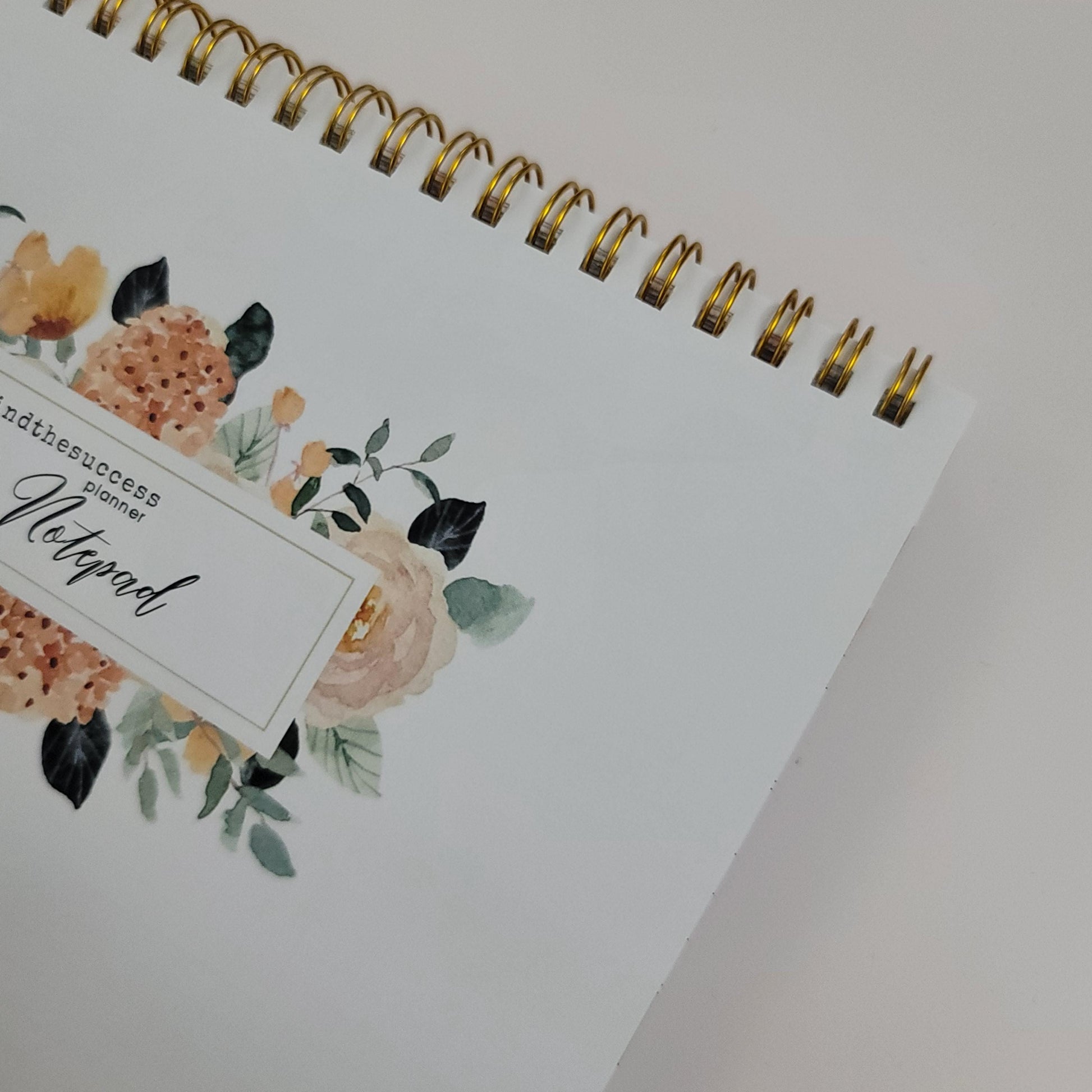 Spiral-bound floral notepad with gold ring binding and elegant flower design on cover