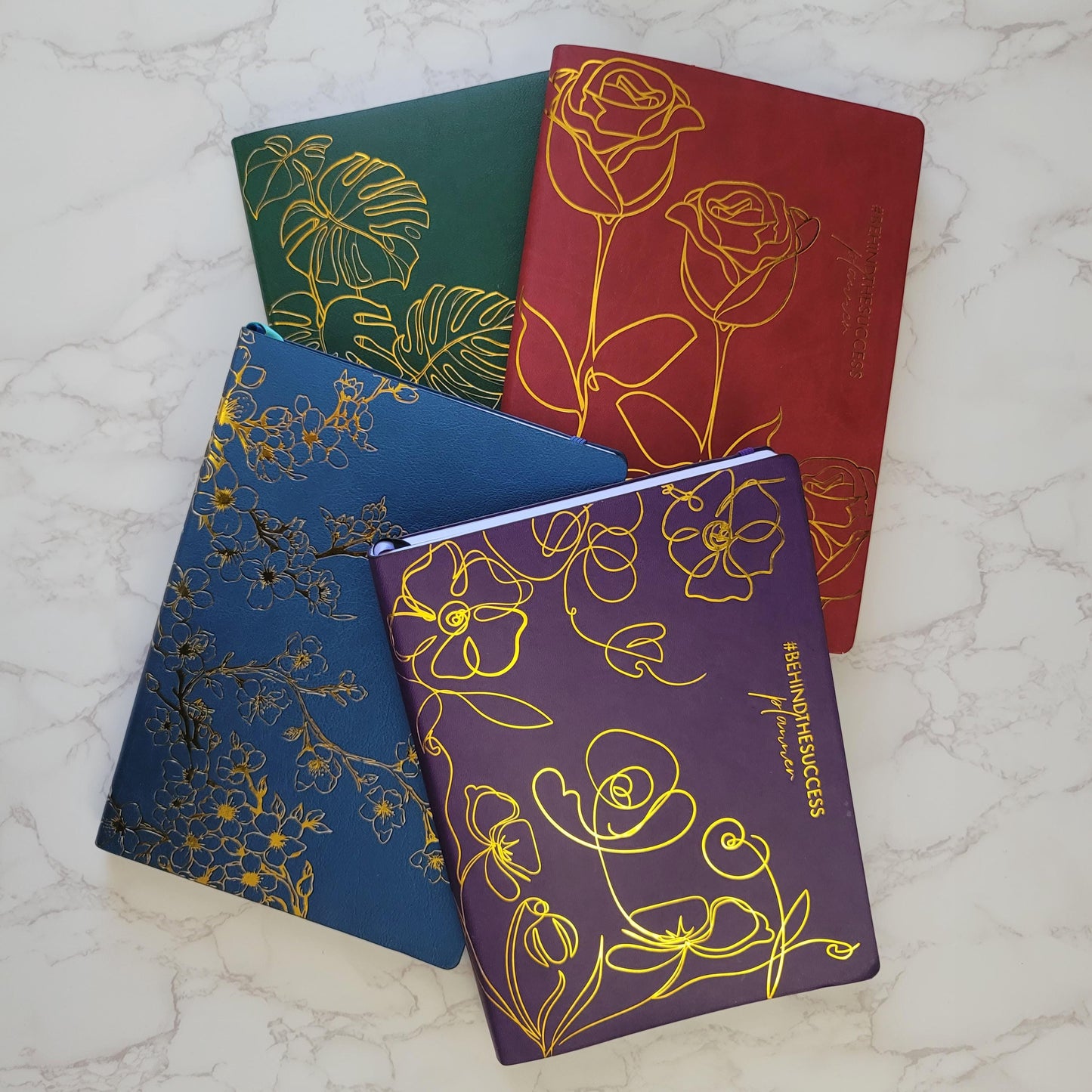 Colorful floral-embossed planners with gold foil on marble background, productivity journals