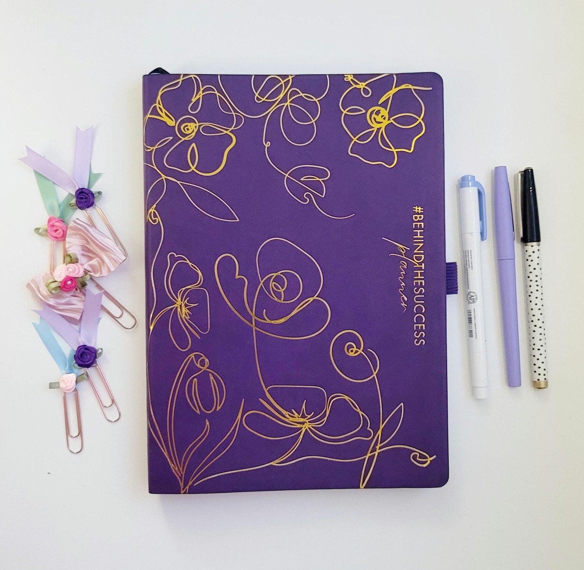 Purple undated productivity planner with gold floral design, pens, and decorative paper clips